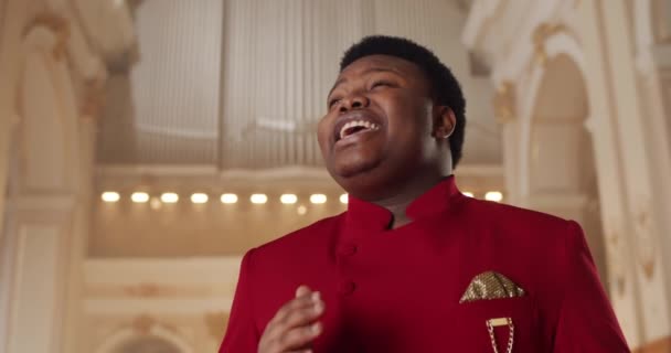 Genç Afro-Amerikan bir adamın duygusal olarak şarkı söyleyip el ele tutuşmasını yakından çek. Protestan kilisesinde kırmızı elbiseli erkek ruhani şarkıcı. Din kavramı. — Stok video