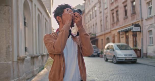 Millenniumi férfi orrkarikával fotózza a városi tájat. Jóképű férfi turista szemüvegben áll a régi városi utcában. Az utazás, a turizmus és a fotográfia fogalma. — Stock videók