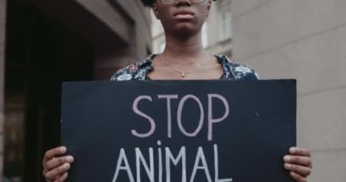 Üzerinde hayvan istismarı yazan karton pankart tutan Afro-Amerikan genç bir kadın. Milenyum kızı şehir caddesinde dururken hayvan hakları hareketlerini destekliyor..
