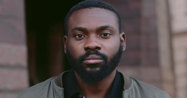 Vista de perto do cara barbudo afro-americano olhando para a câmera com expressão facial séria. Retrato de homem bonito jovem em pé na rua da cidade.Conceito de pessoas e emoções . — Vídeo de Stock