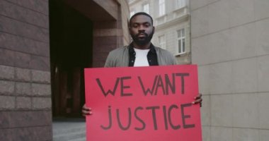 Elinde pankart tutan aktivistin portresi. Üzerinde adalet yazısı olsun istiyoruz. Afro-Amerikan sakallı adam boş şehir caddesinde dururken insan hakları hareketini destekliyor..