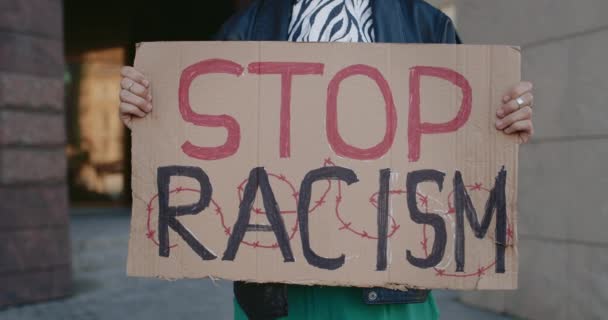 Close up view of womans hands holding no to racism phrase cardboard at city street. Female actibist supporting anti racism campaign. Concept of equal human rights. — Stock Video