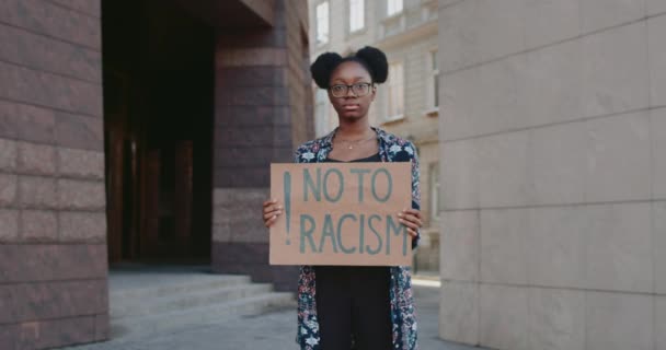 African american girl holding no to racism phrase cardboard while standing at city street. Student supporting anti racism campaign. Concept of equal human rights. Zoom in. — Stock Video