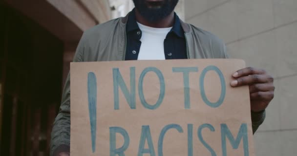 Vue rapprochée d'un militant afro-américain tenant une pancarte en carton sans racisme écrivant dans la rue de la ville. Concept des droits de l'homme et de l'inégalité raciale. — Video