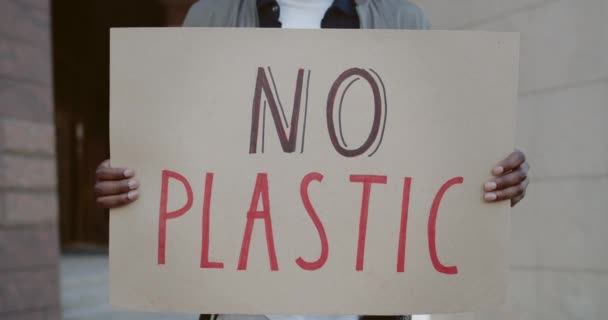 Afro american male supporting ecology movement. Close up of hands holding carton placard with no plastic slogan and standing at city street. Concept of environmental pollution. — Stock Video