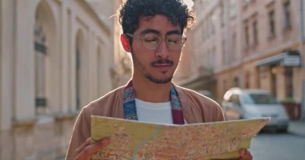 Turista masculino milenario con anillo en la nariz mirando el mapa y que en el monumento frente a él. Un tipo guapo con gafas parado en la vieja calle de la ciudad. Concepto de viaje y turismo . — Vídeos de Stock