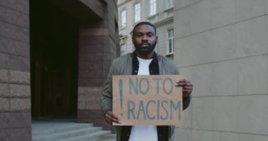 Elinde ırkçılığa hayır tabelası tutarken kameraya bakan Afro-Amerikan bir adamın portresi. Sakallı adam şehir sokaklarında ırksal eşitsizliği protesto ediyor. İnsan hakları kavramı.