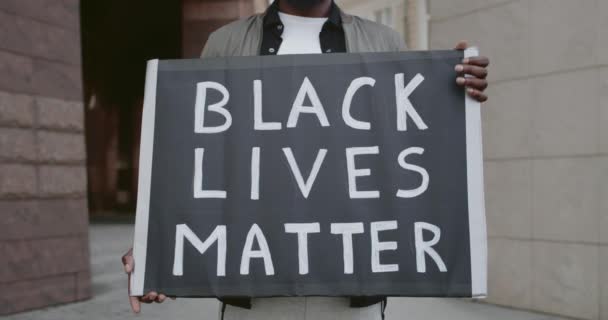 アフリカ系アメリカ人男性の手を黒の生活物質を書くとカートンのプラカードを保持。街中に立ち警察の残虐行為や人種差別に反対する運動を支援する活動家. — ストック動画