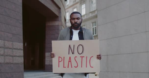 En ung afrikansk amerikan utan plastaffisch på gatan. Skäggiga manliga aktivister som stöder ekologstrejkrörelsen. Begreppet miljöförstöring och rädda jorden. Zooma in. — Stockvideo