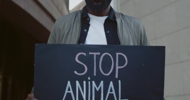 Portrait d'un jeune homme afro-américain tenant une pancarte en carton sur laquelle figure un écriteau pour empêcher les abus d'animaux. Homme millénaire soutenant les mouvements de défense des droits des animaux alors qu'il se tenait dans la rue. — Video