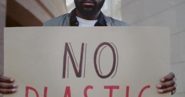 アフリカ系アメリカ人の男性のエコ活動家は、プラスチック製の書き込みなしでカートンのプラカードを保持。街の通りに立っている間、生態系の動きを支える若い男。環境意識の概念. — ストック動画