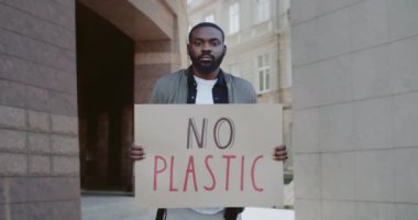 Şehir caddesinde plastik karton pankartı olmayan ciddi bir Afro-Amerikan adamın portresi. Genç adam çevreci grev hareketini destekliyor. Çevre kirliliği kavramı.