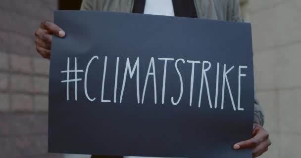 Manos masculinas afroamericanas sosteniendo cartel de cartón con etiqueta de huelga climática en la calle de la ciudad. Activista en huelga por la ecología y el planeta limpio. Concepto de salvar la Tierra . — Vídeos de Stock
