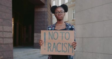 Elinde ırkçılığa hayır tabelasıyla kameraya bakan Afrikalı Amerikalı bir kızın portresi. Burun halkalı kadın şehir sokaklarında ırksal eşitsizliği protesto ediyor. İnsan hakları kavramı.