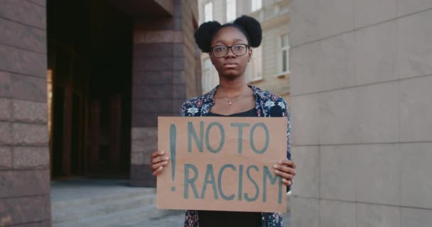 Portret van een Afrikaans Amerikaans meisje dat naar de camera kijkt terwijl ze een bord met nee houdt tegen racisme. Vrouw met neusring protesteert tegen rassenongelijkheid op straat. Begrip mensenrechten. — Stockvideo