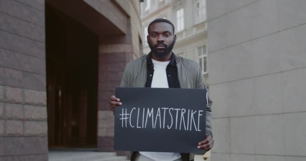Вид на людину, яка тримає картонний плакат з хештегом кліматичного страйку, стоячи на міській вулиці. Красивий хлопець підтримує рух за екологію та чисту планету. Концепція порятунку Землі . — стокове відео