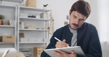 Bıyıklı, tabletli ve çizimli bir erkek grafik tasarımcısı. Yakışıklı adam, günlük giysiler giyiyor. Resim oluştururken dokunuyor ve yakınlaştırıyor..