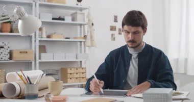 Tablete resim çizen ve rahat çalışma yerinde resim çizen yakışıklı adam. Yeni proje üzerinde çalışırken stilus ve not defteri kullanan genç adam grafik çizer..