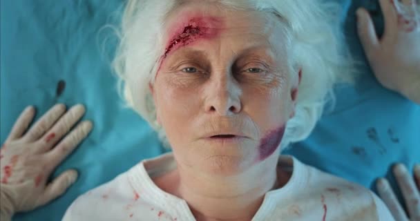 血液や頭の傷を持つ成熟した女性のトップビューは、病院に救急車に乗って。救急車の医療輸送車の上に寝そべっている負傷した老婦人の終わり。医療の概念. — ストック動画
