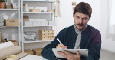 Elinde not defteri olan ve üzerinde stilus olan genç bir adam. Bıyıklı yaratıcı bir adam dijital tablet tutarken resimleme yapıyor ve rahat bir iş yerinde oturuyor. Sanat anlayışı..