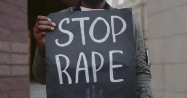 Afro-Amerikan erkeklerin ellerinde karton levhalarla şehir caddesinde tecavüz yazılarını durdurmalarını yakından izleyin. Şiddete ve saldırıya karşı hareketi destekleyen eylemci.
