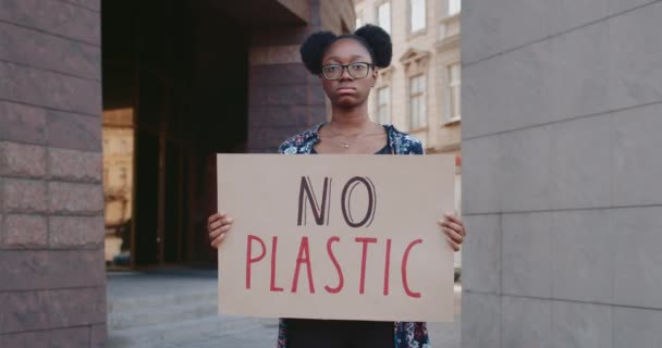 Portrait of serious african american woman with no plastic carton banner standing at city street. Millennial girl supporting ecology strike movement. Concept of environmental pollution. — Stock Video