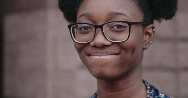 Портрет молодої афро-американської дівчини посміхається, дивлячись на камеру. Згорнути красиву тисячолітню жінку з радісним виразом обличчя. Концепція емоцій. Розмите тло. — стокове відео