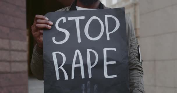 Närbild av afrikanska amerikanska manliga händer som håller kartongplakat med stopp våldtäkt skriva på stadens gata. Aktivist som stöder rörelse mot våld och misshandel. — Stockvideo