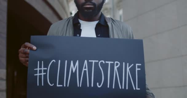 Nauwe blik op de jonge serieuze man die milieubescherming steunt. Afro-Amerikaanse man met klimaatvlag terwijl hij op straat stond. Begrip ecologie. — Stockvideo