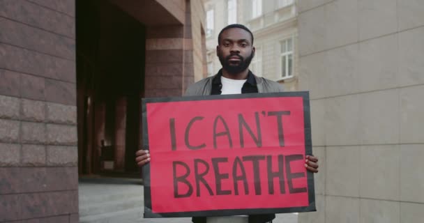 Retrato de un activista afroamericano con pancarta y sin aliento. Tipo guapo apoyando el movimiento contra la violencia y el racismo mientras está parado en la calle de la ciudad . — Vídeo de stock