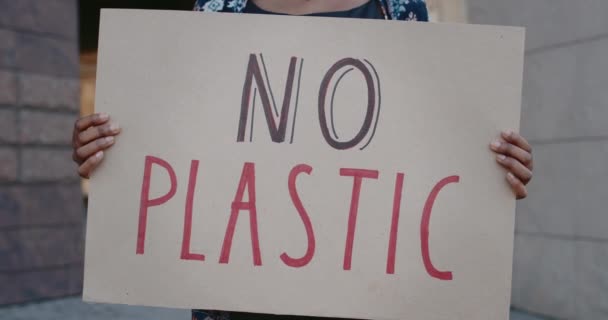 Close up of hands holding carton placard with no plastic slogan and standing at city street. Afro american female supporting ecology movement. Concept of environmental pollution. — Stock Video