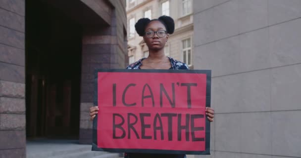 Portret afrykańskiej aktywistki trzymającej plakietkę z zapierającym dech w piersiach napisem. Millenijna dziewczyna wspiera ruch przeciwko przemocy i rasizmowi stojąc na ulicy miejskiej. — Wideo stockowe