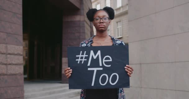 Retrato de una estudiante en gafas sosteniendo pancarta con MeToo escribiendo en la calle de la ciudad. Niña afroamericana que apoya el movimiento contra el acoso sexual. Concepto de problemas sociales . — Vídeo de stock