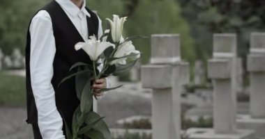 Genç bir delikanlının, babasının mezar taşına beyaz zambak koyduğu yakın plan. Genç bir çocuk mezarlıkta babasının askerini onurlandırıyor. Anma Günü kavramı.