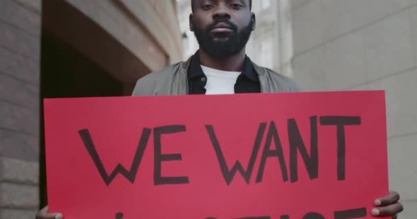 Podívejte se zblízka na Afroameričana, jak drží prapor s nápisem spravedlnost. Mužský aktivista podporující hnutí proti brutalitě a rasismu, když stojí na ulici.