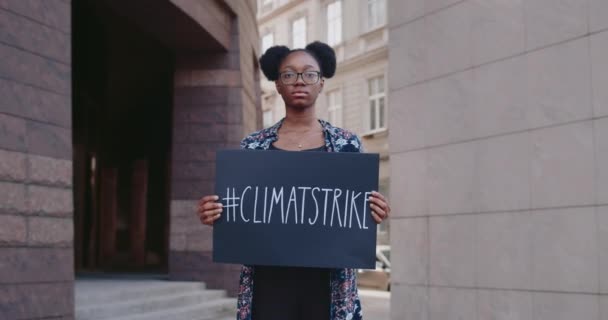 Afro american woman holding placard with climate strike hashtag while standing at city street. Millennial girl striking for ecology and clean planet. Concept of save Earth. Zoom in. — Stock Video