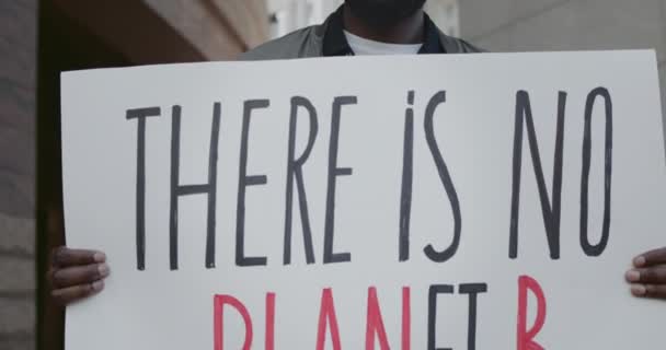 Vista de cerca de los manifestantes masculinos sosteniendo pancarta con no hay planeta b escritura. Activista afroamericano que apoya el movimiento ecológico mientras hace una sola protesta en la calle de la ciudad . — Vídeo de stock