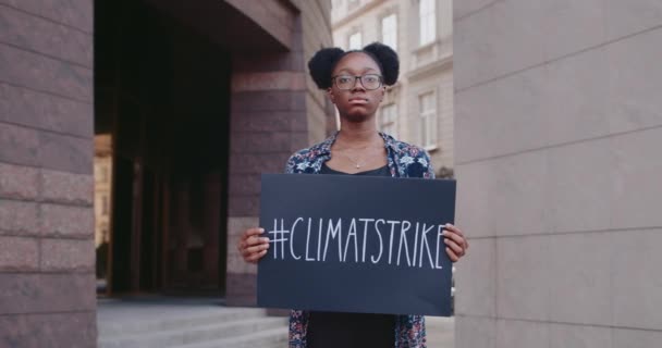 Egy afro-amerikai nő portréja, aki kartondobozt tart klíma sztrájk hashtaggel a City Streeten. A lány támogatja az ökológiát és a tiszta bolygót. A Föld megmentésének koncepciója. — Stock videók