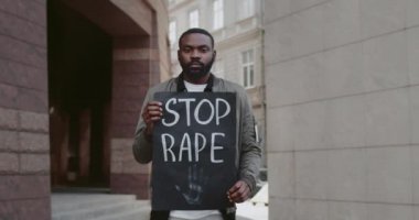 Afro-amerikalı bir adam elinde karton bir plân tutuyordu. Şehir caddesinde tecavüzü durdurun yazıyordu. Erkek protestocu şiddete ve saldırıya karşı hareketi destekliyor. Sosyal sorunlar kavramı. Yakınlaştır.