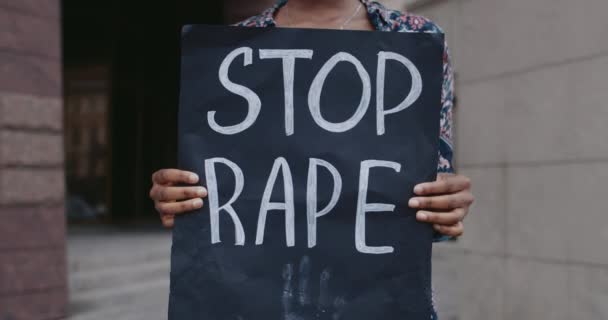 Pandangan dekat african american tangan perempuan memegang karton plakat dengan berhenti pemerkosaan menulis di jalan kota. Aktivis mendukung gerakan melawan kekerasan dan penyerangan. — Stok Video