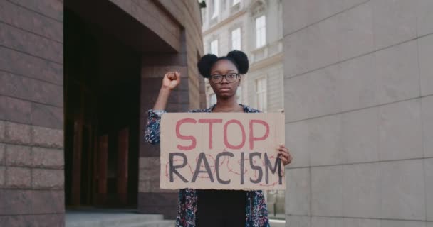 African american girl raising up clintched fist and holding carton cardbord with stop racism. Activist supporting equal human rights movement while standing at city street.Zoom in. — Stock Video