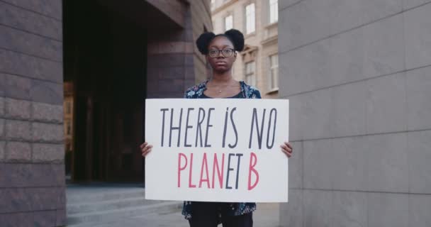 Niña afroamericana joven sosteniendo que no hay planeta b de cartón, mientras que de pie en la calle de la ciudad. Acrivista femenina que apoya la campaña ecológica. Concepto de protección ambiental. Acercar. — Vídeos de Stock