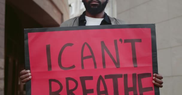 Африканский активист-американец держит плакат, на котором я не могу дышать. Бородатый парень поддерживает движение против полицейской жестокости и расизма, стоя на улице. — стоковое видео
