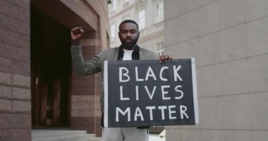 Yakışıklı sakallı adam elinde siyah hayatlar yazılı bir karton levha tutuyor. Genç Afrikalı Amerikalı adam sokakta dururken ırkçılığa karşı hareketi destekliyor. Yakınlaştır.