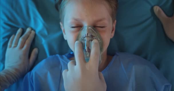 Κοντινό πλάνο ασυνείδητου παιδιού με μάσκα εισπνοής οξυγόνου ξαπλωμένη σε ιατρικό φορείο. Οι νοσοκόμοι ελέγχουν τον σφυγμό και κάνουν καρδιακό μασάζ στο αγοράκι ενώ πηγαίνουν στο νοσοκομείο.. — Αρχείο Βίντεο