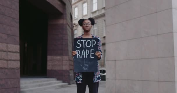 Afrikansk amerikansk tjej med kartong och sluta skriva våldtäkt på City Street. Kvinnlig student som stödjer rörelse mot våld och misshandel. Begreppet sociala problem. Zooma in. — Stockvideo