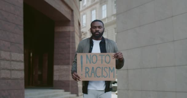 African american guy holding no to racism phrase cardboard while standing at city street. Bearded man supporting anti racism campaign. Concept of equal human rights. Zoom in. — Stock Video