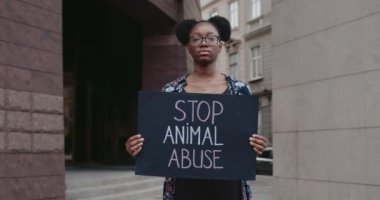 Afro-Amerikalı kadın elinde hayvan istismarı yazılarını durduran bir karton levha tutuyor. Sokakta kameraya bakan kadın hayvan hakları savunucusunun portresi. Sosyal sorun kavramı.