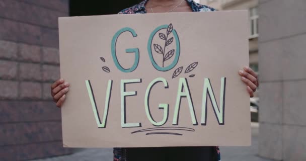 Afrikanska amerikanska kvinnliga händer håller Gå vegan tecken när du står på gatan. Närbild av kvinna främja vegetarianism och hälsosam livsstil. Begreppet Go Green och eko. — Stockvideo