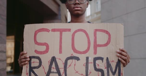 Close-up van het meisje in haar handen te stoppen racisme frase karton. Vrouwelijke Afro-Amerikaanse student steunt anti-racisme campagne in de stad straat. Begrip gelijke mensenrechten. — Stockvideo